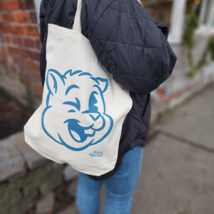 A woman stands on a sidewalk with a tote bag slung over her shoulder, an image of a winking cartoon squirrel on the tote.